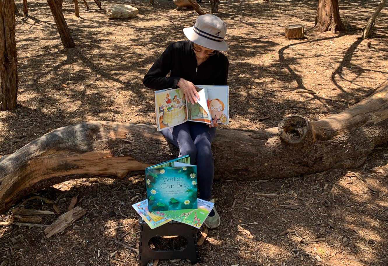 Woman sitting on a log, showing a picture book, while turning to the next page. 